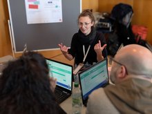 Eine Workshopreferentin erklärt engagiert den Interviewbot vor Teilnehmenden an einem Tisch im Seminarraum.